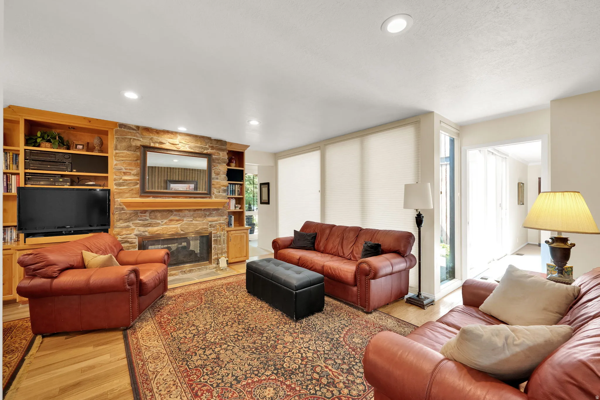 Living area featuring a stone fireplace with a wood mantel, built-in shelving, wood-finish flooring, recessed lighting, and large windows