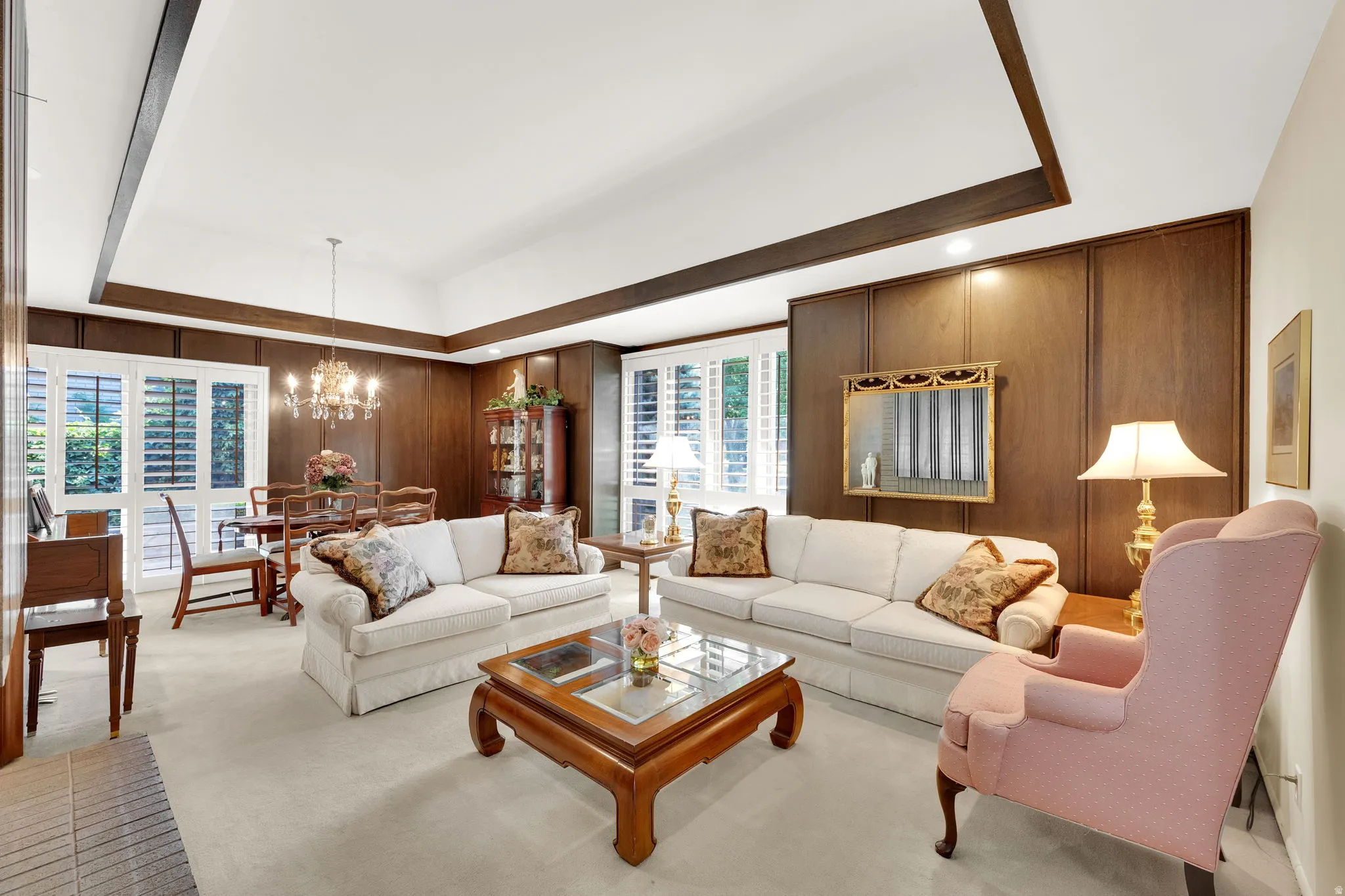 Spacious living area featuring coffered ceilings, wood-paneled walls, and plush carpeting