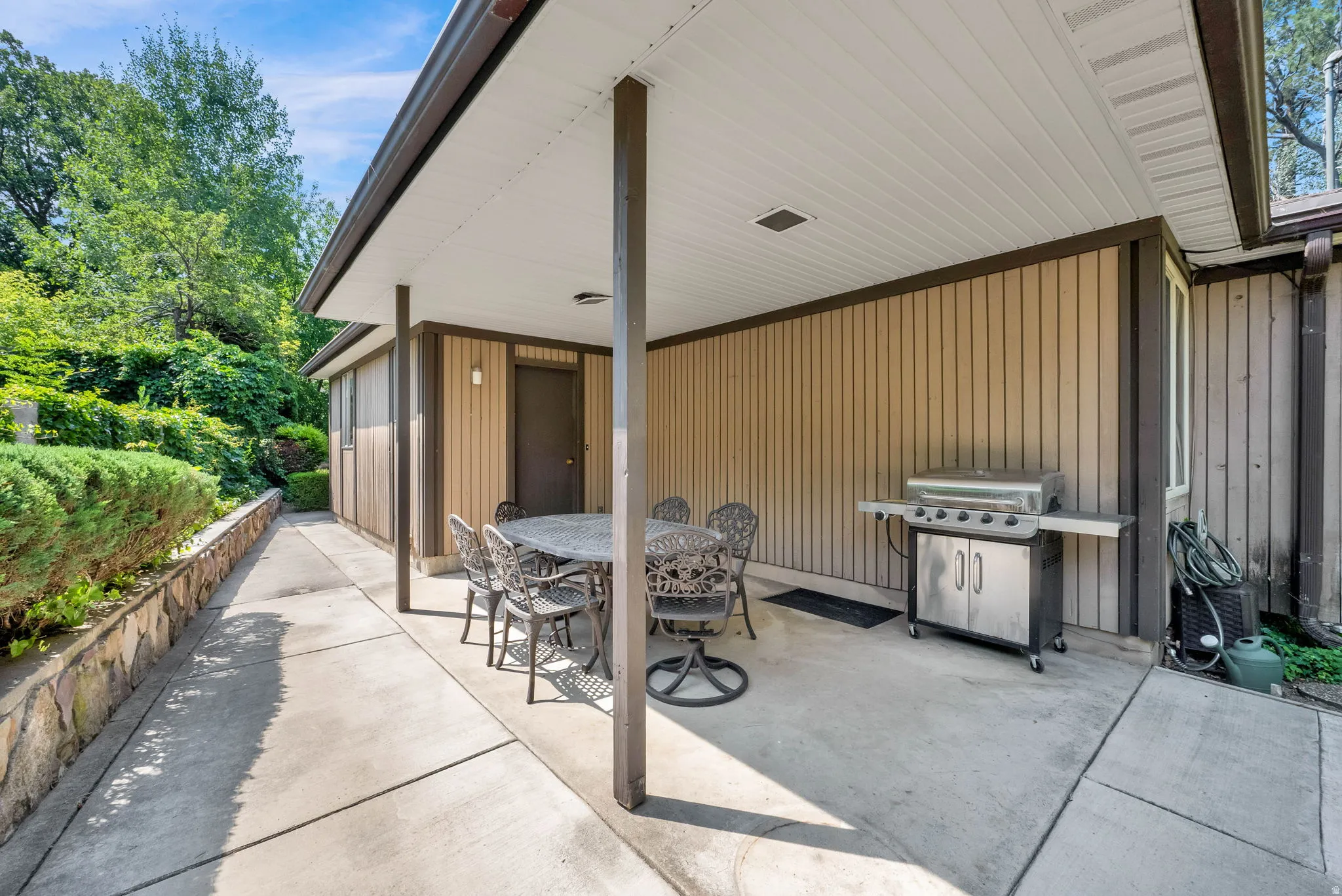 Covered concrete patio with vertical plank siding and a stone-faced retaining wall