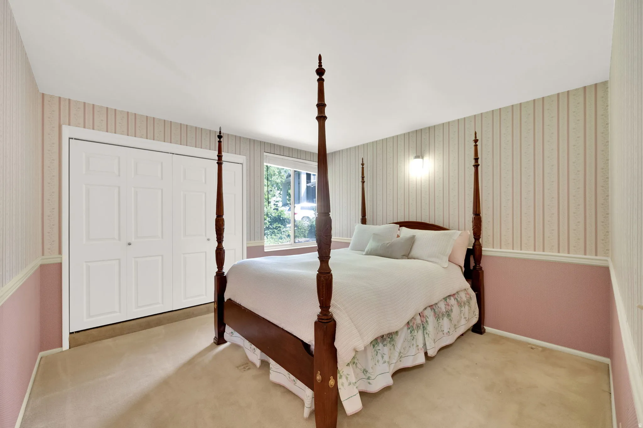 Plush carpet flooring complements a neutral wall palette with a striped upper and a solid lower section, featuring a window and bi-fold closet doors