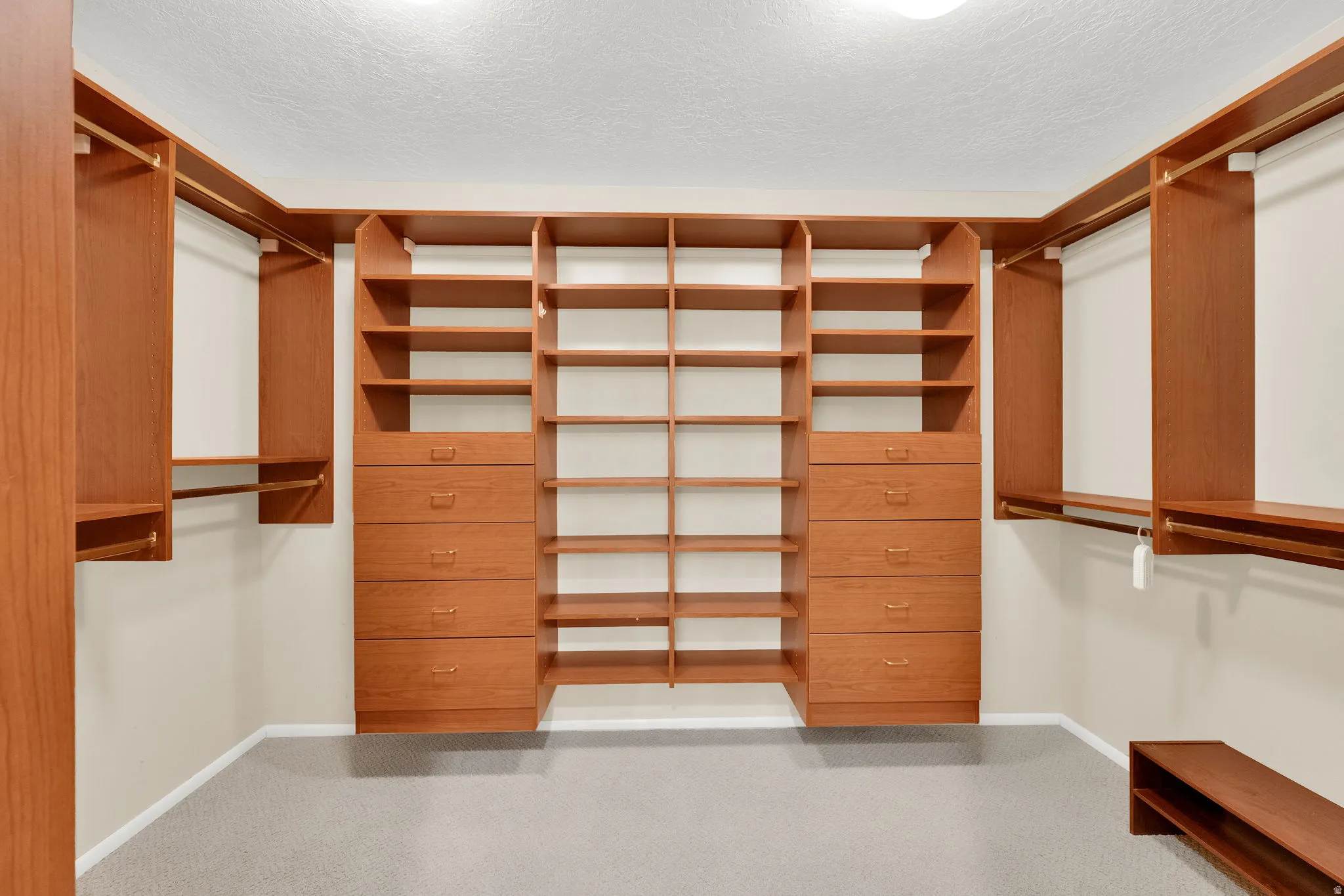 Custom closet system featuring wood-finish cabinetry, ample shelving, integrated drawers, multiple hanging rods, and light gray carpet flooring