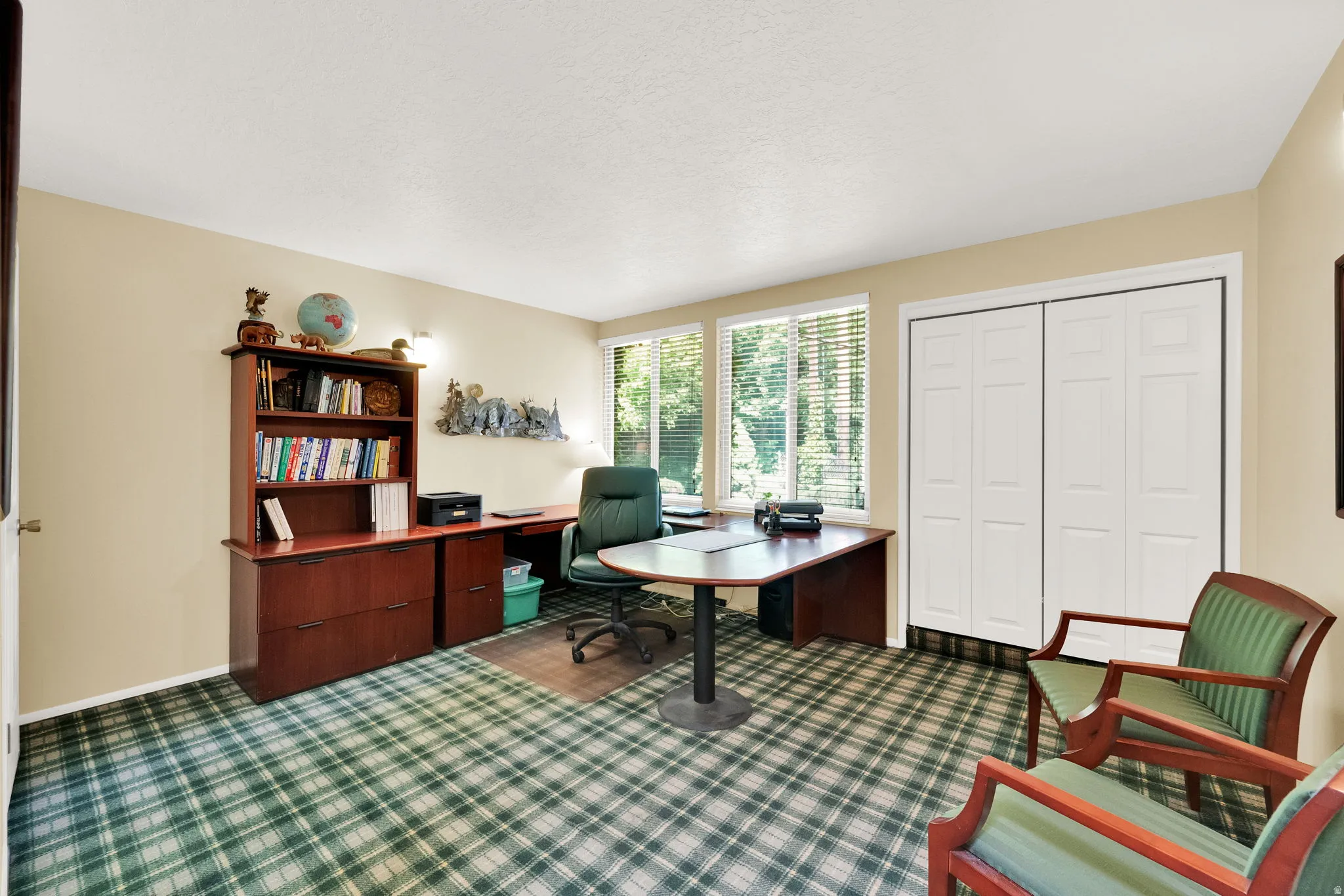 Room featuring patterned carpet flooring, neutral painted walls, and abundant natural light from multiple windows.  Used as an office could be a large bedroom.  Two closets.