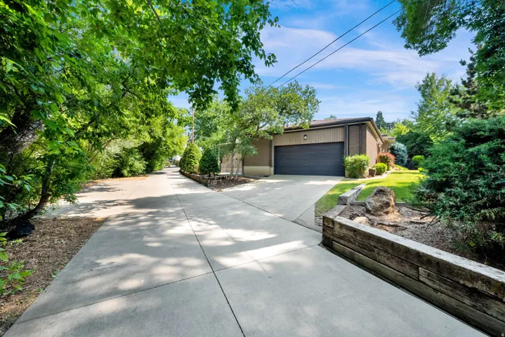 Paved driveway with mature trees, a dark paneled garage door, and an exterior featuring brown vertical siding and brick accents