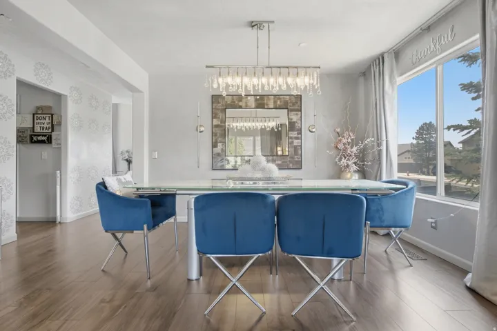 Spacious dining area featuring wood-finish flooring, a contemporary chandelier, a large window, and light-colored walls