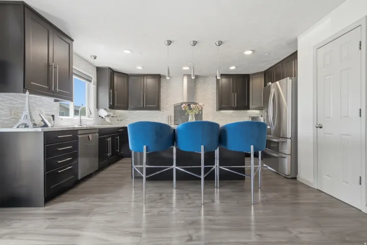 Contemporary kitchen featuring dark wood-finish cabinetry, stainless steel appliances, a center island with pendant lighting, a tile backsplash, and light wood-finish flooring