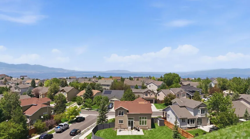 Residential neighborhood with established homes, mature trees, and a distant body of water framed by mountains