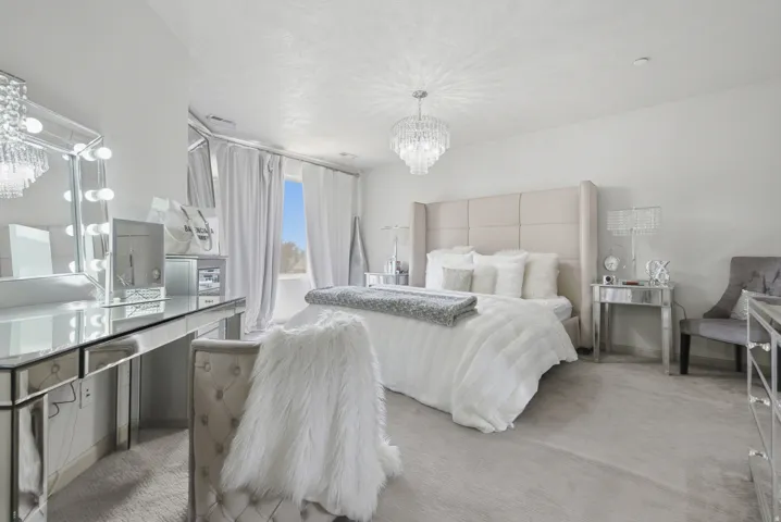 Spacious room featuring a tufted upholstered headboard, mirrored vanity with integrated lighting, and a crystal chandelier