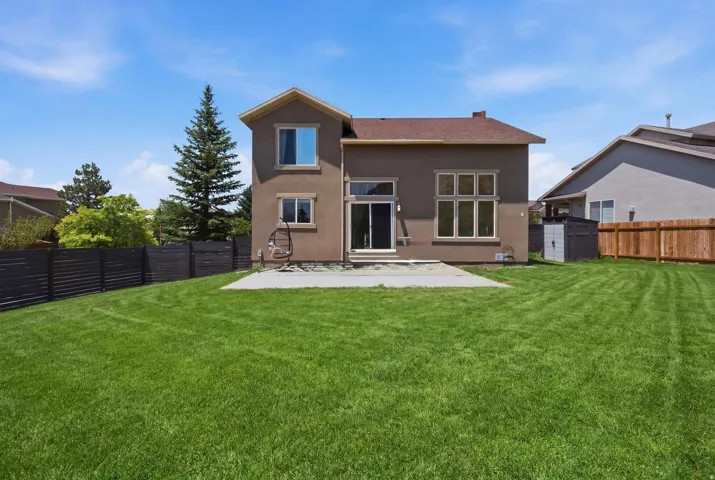 Expansive green lawn with a stucco exterior, featuring a sliding glass patio door, a rectangular concrete patio, and a privacy fence