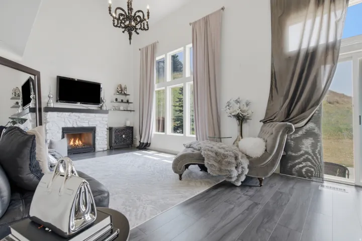 Living space featuring high vaulted ceilings, a stone-clad fireplace, dark wood-finish flooring, and large windows with abundant natural light