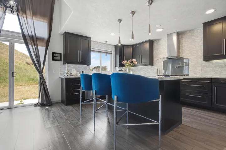 Contemporary kitchen featuring dark cabinetry, a light-toned tile backsplash, and a central island with pendant lighting