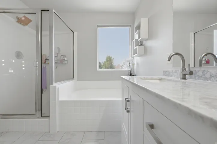 Bathroom featuring a spacious soaking tub, glass-enclosed shower, dual vanity with undermount sinks, stone-finish countertops, and wood-finish flooring