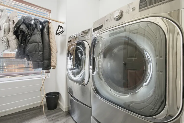 Dedicated laundry area featuring front-loading appliances, wood-finish flooring, and a large window with blinds
