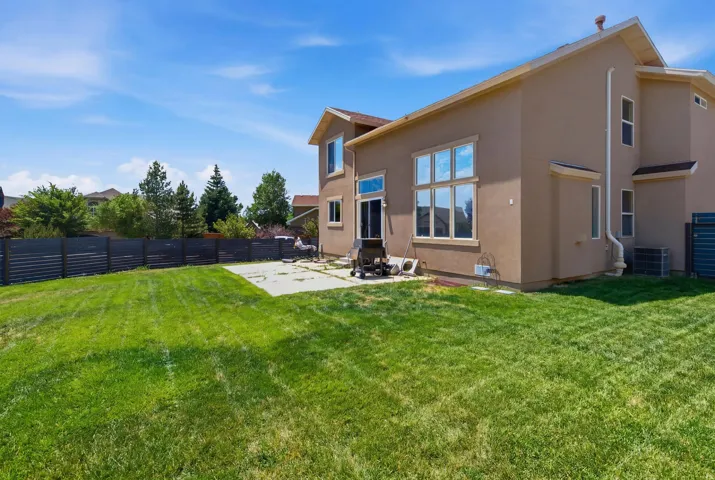Expansive backyard featuring a manicured lawn, full stucco exterior, multiple large windows, and a concrete patio