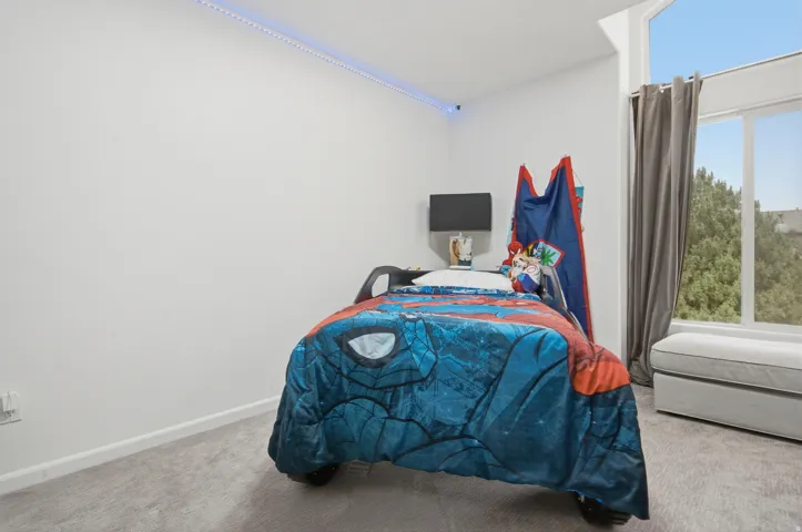 Room featuring a large window with an angled transom, light gray carpeting, white walls, and a built-in wall-mounted light fixture