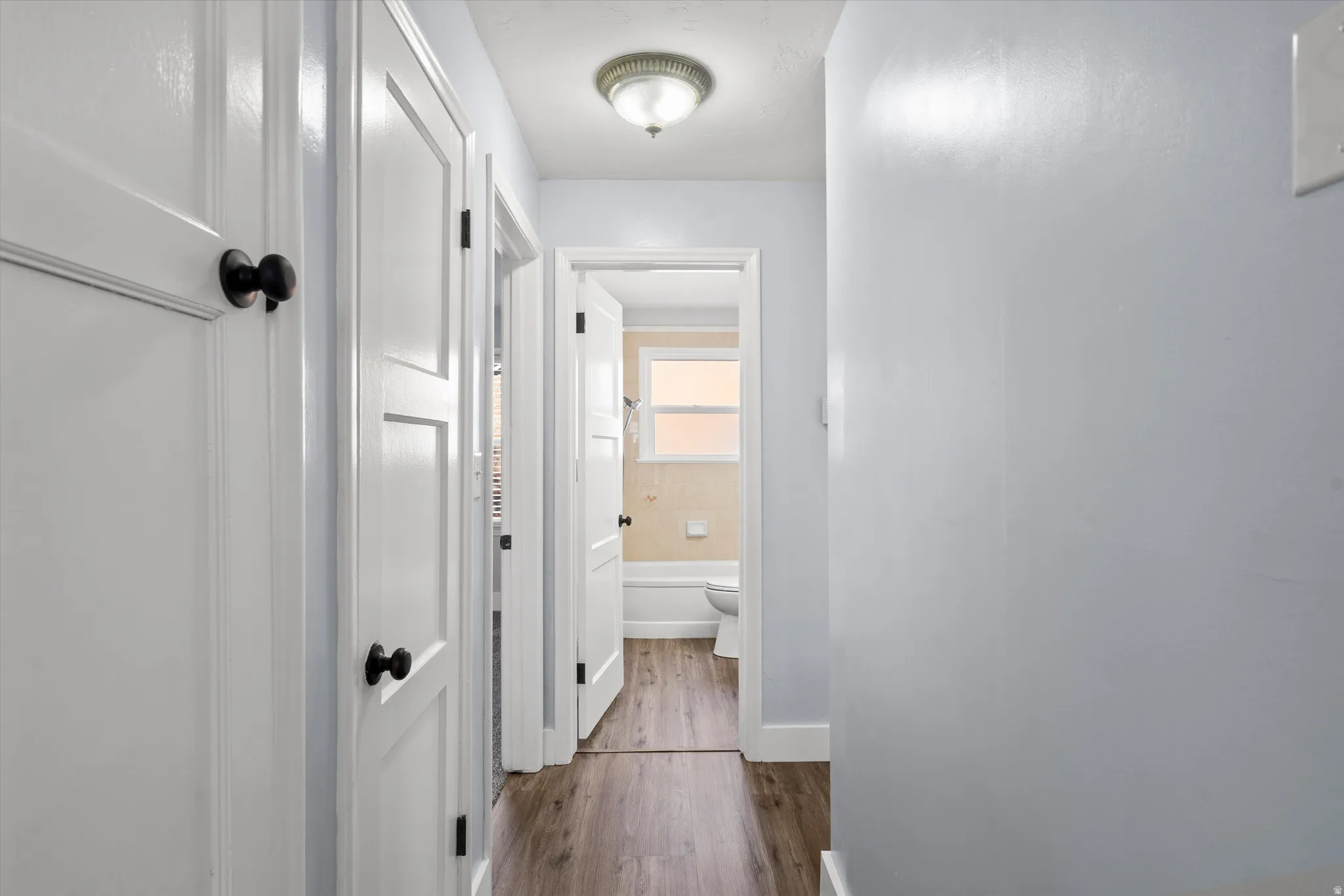 Hallway featuring wood-finish flooring and multiple white panel doors with black hardware