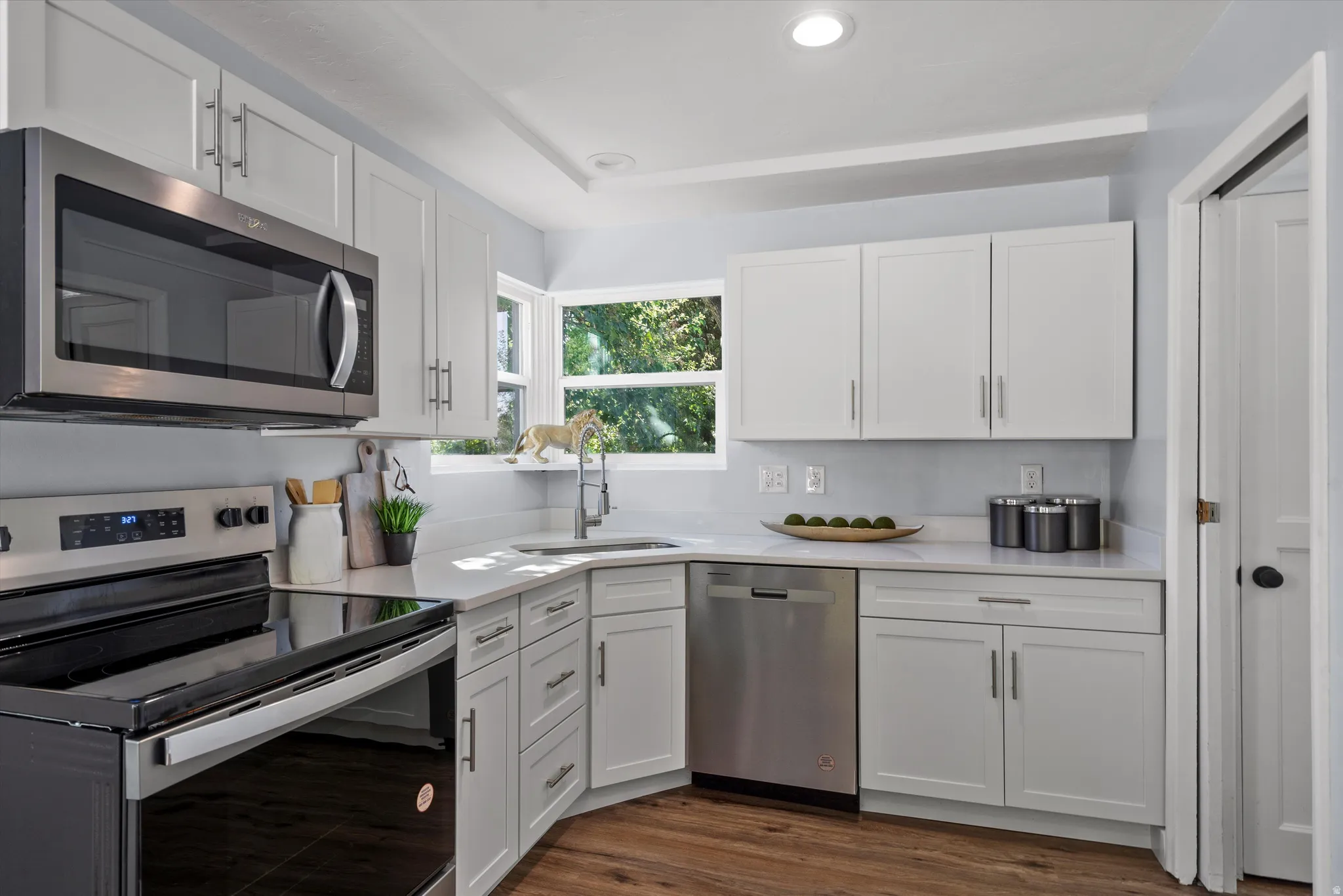 Modern kitchen featuring white shaker cabinetry, stainless steel appliances, and wood-finish flooring