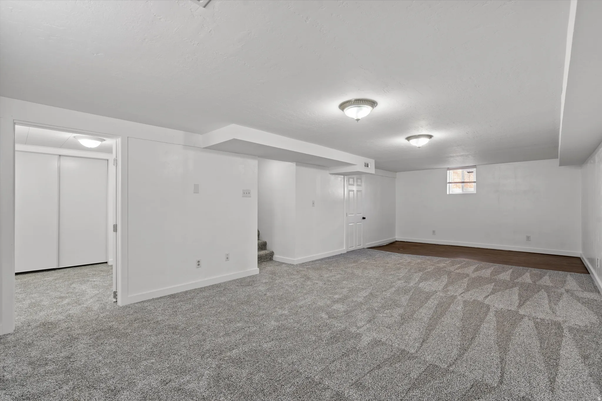 Spacious finished room featuring textured carpeting with geometric patterns, white walls, and flush-mount lighting fixtures