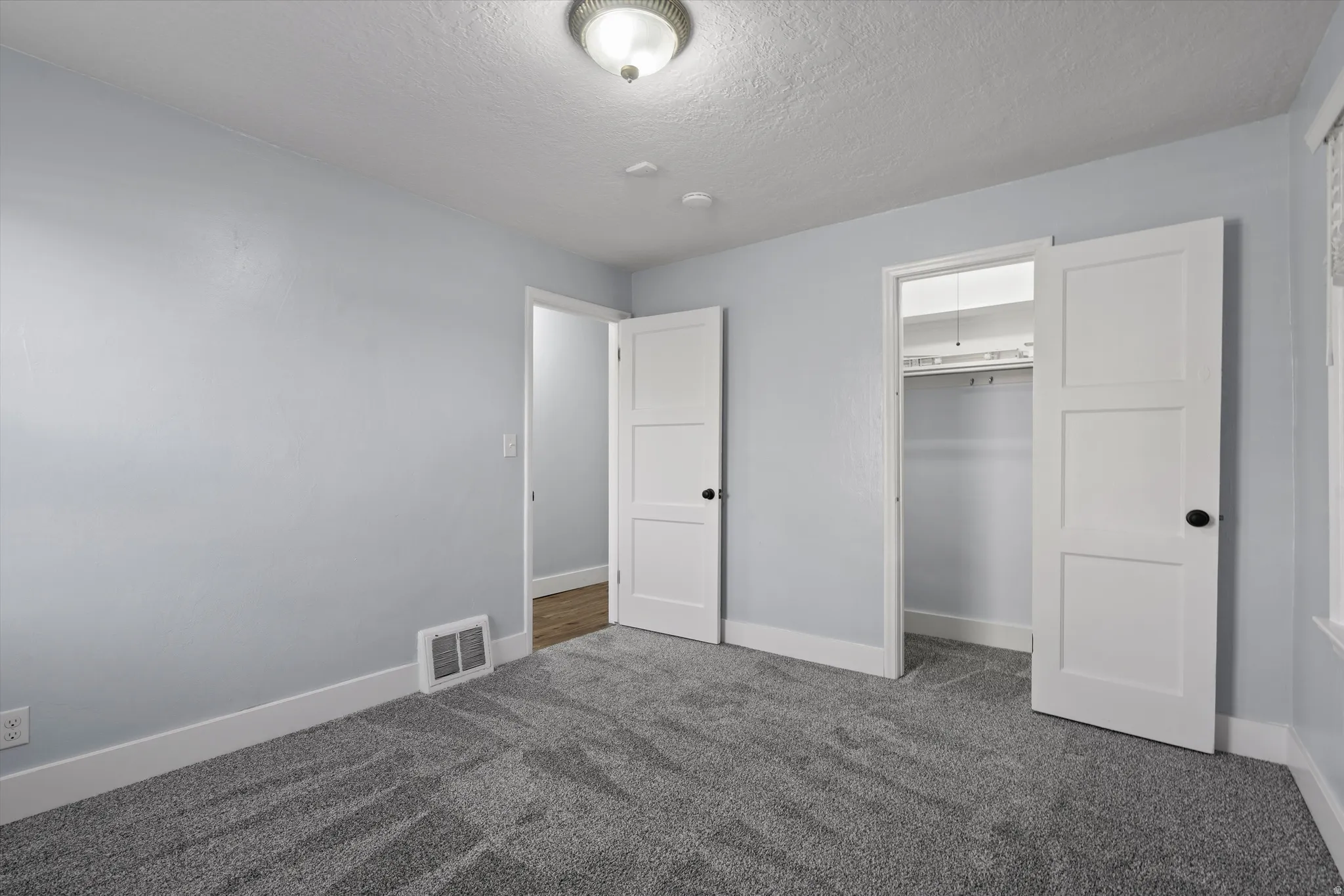 Room featuring grey patterned carpeting, light blue wall paint, white trim, and a white ceiling light fixture