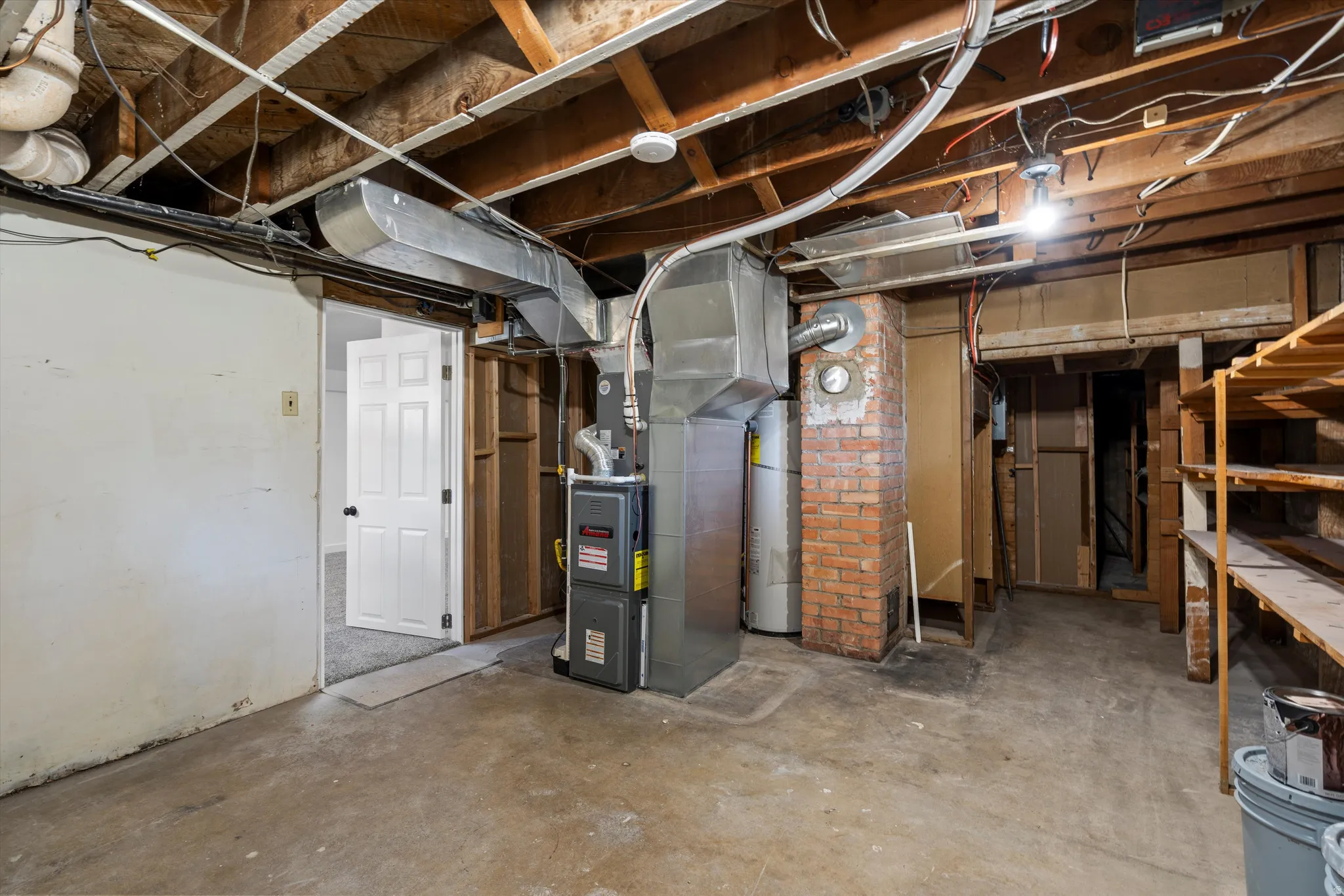 Unfinished basement area featuring exposed ceiling joists, concrete flooring, HVAC system, and brick elements