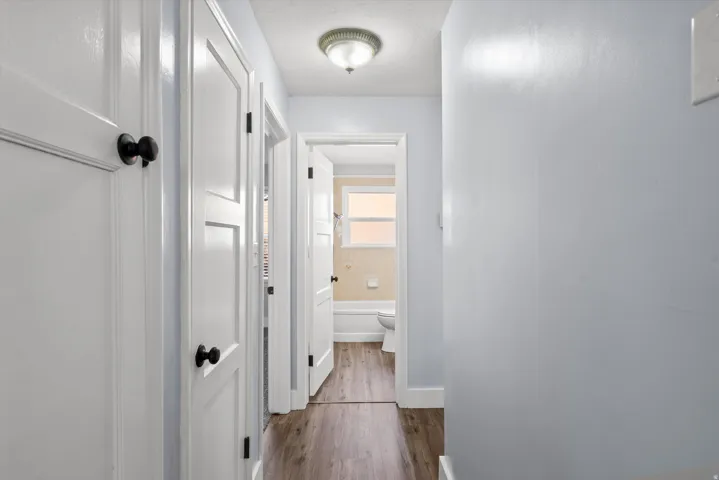 Hallway featuring wood-finish flooring and multiple white panel doors with black hardware