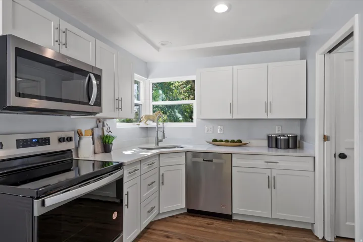 Modern kitchen featuring white shaker cabinetry, stainless steel appliances, and wood-finish flooring