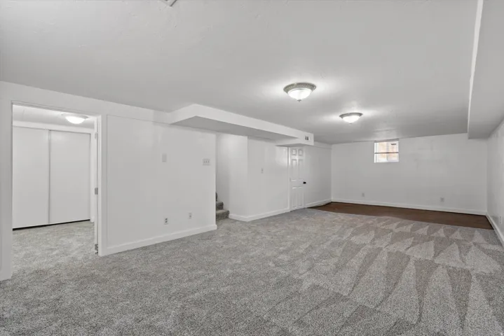 Spacious finished room featuring textured carpeting with geometric patterns, white walls, and flush-mount lighting fixtures