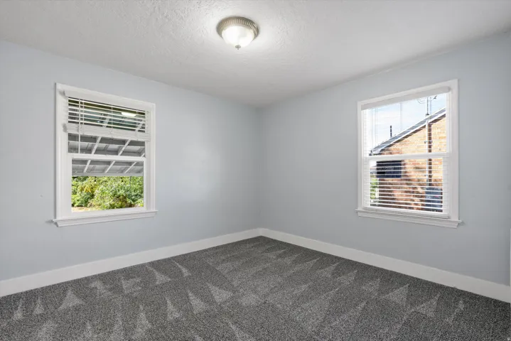 Room featuring light gray walls, patterned gray carpet, and two double-hung windows with white blinds