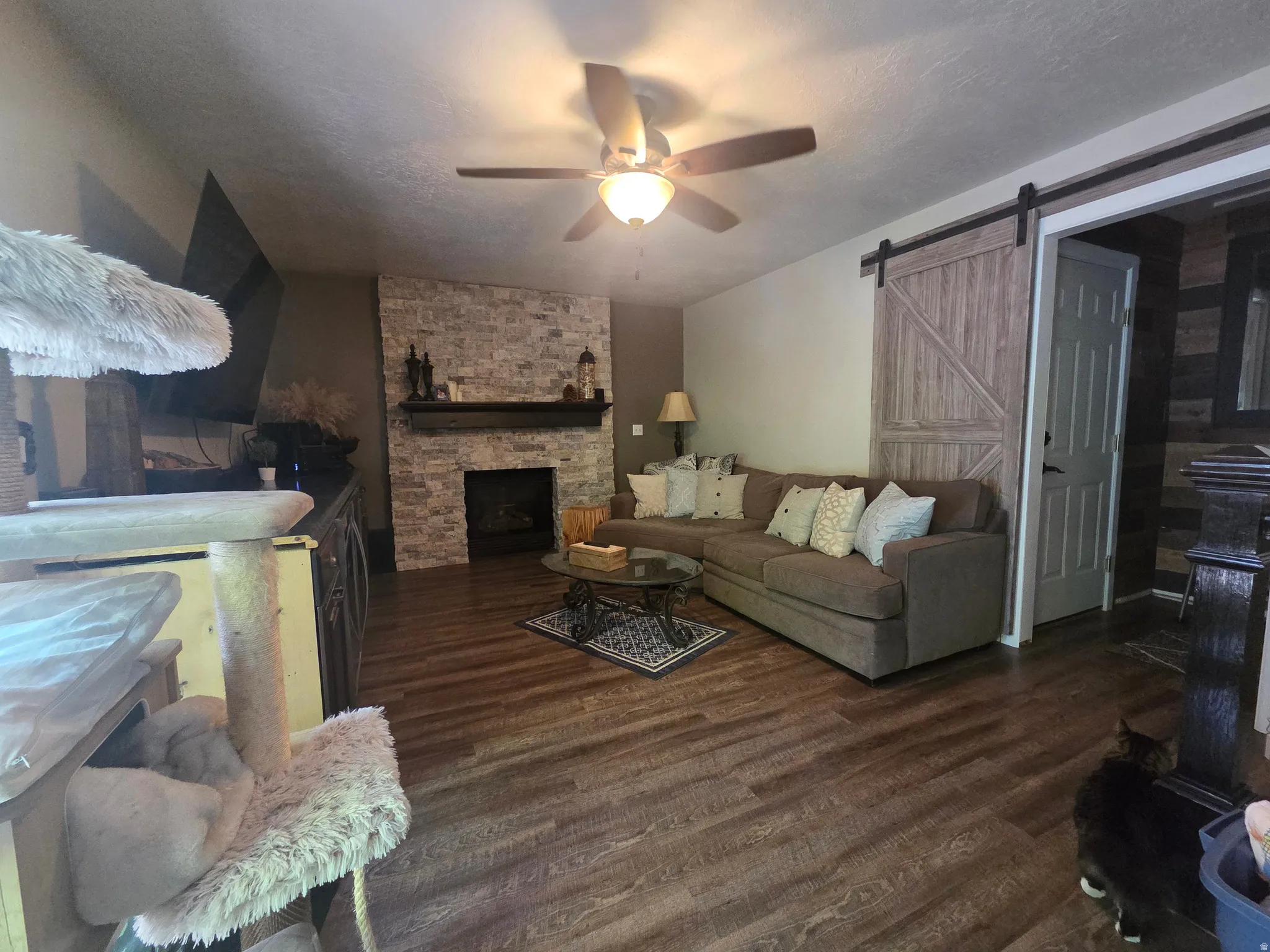 Living area featuring a stone-clad fireplace with a dark wood mantel, wood-finish flooring, and a ceiling fan with integrated lighting
