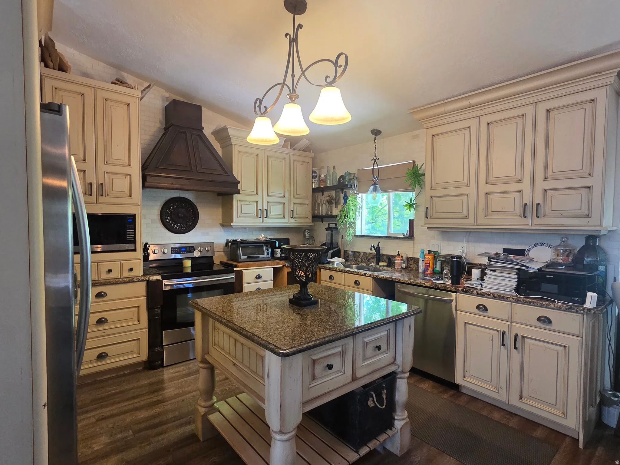 Spacious kitchen featuring an island with a granite countertop, warm-toned cabinetry, stainless steel appliances, and wood-finish flooring