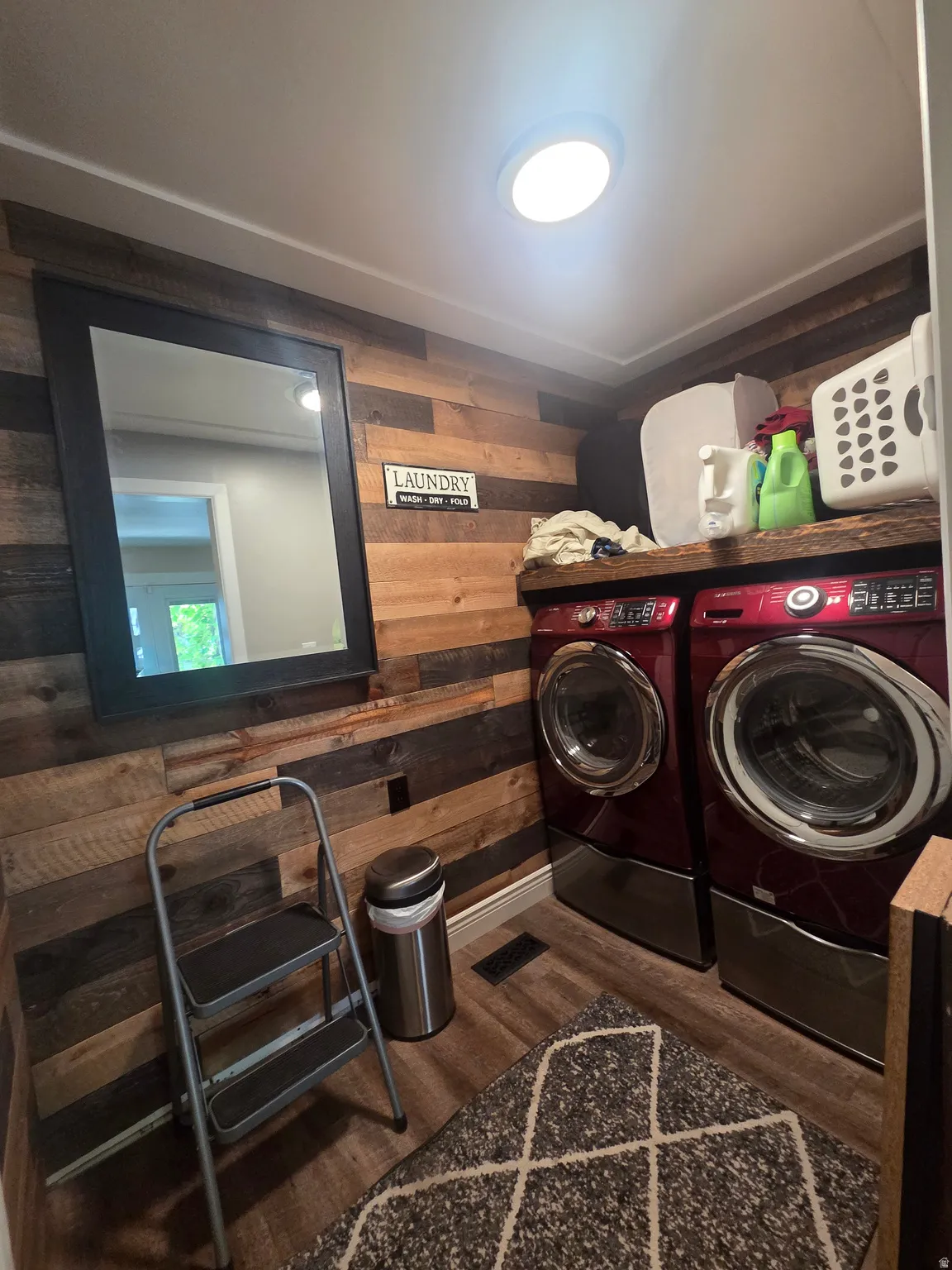 Laundry area featuring wood-panel accent wall and wood-finish flooring