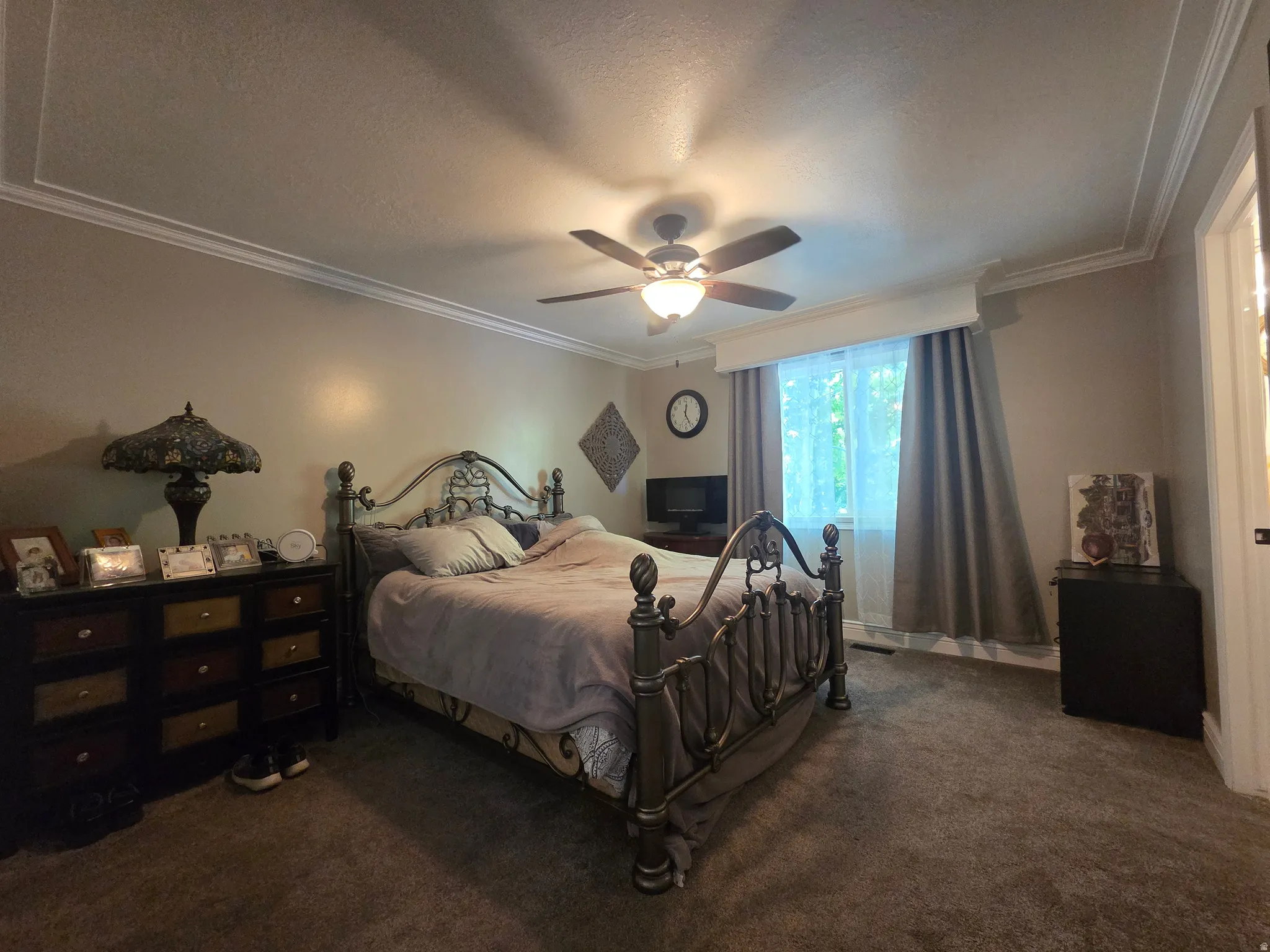 Spacious bedroom featuring plush carpeting, a ceiling fan with integrated lighting, and a window with valance