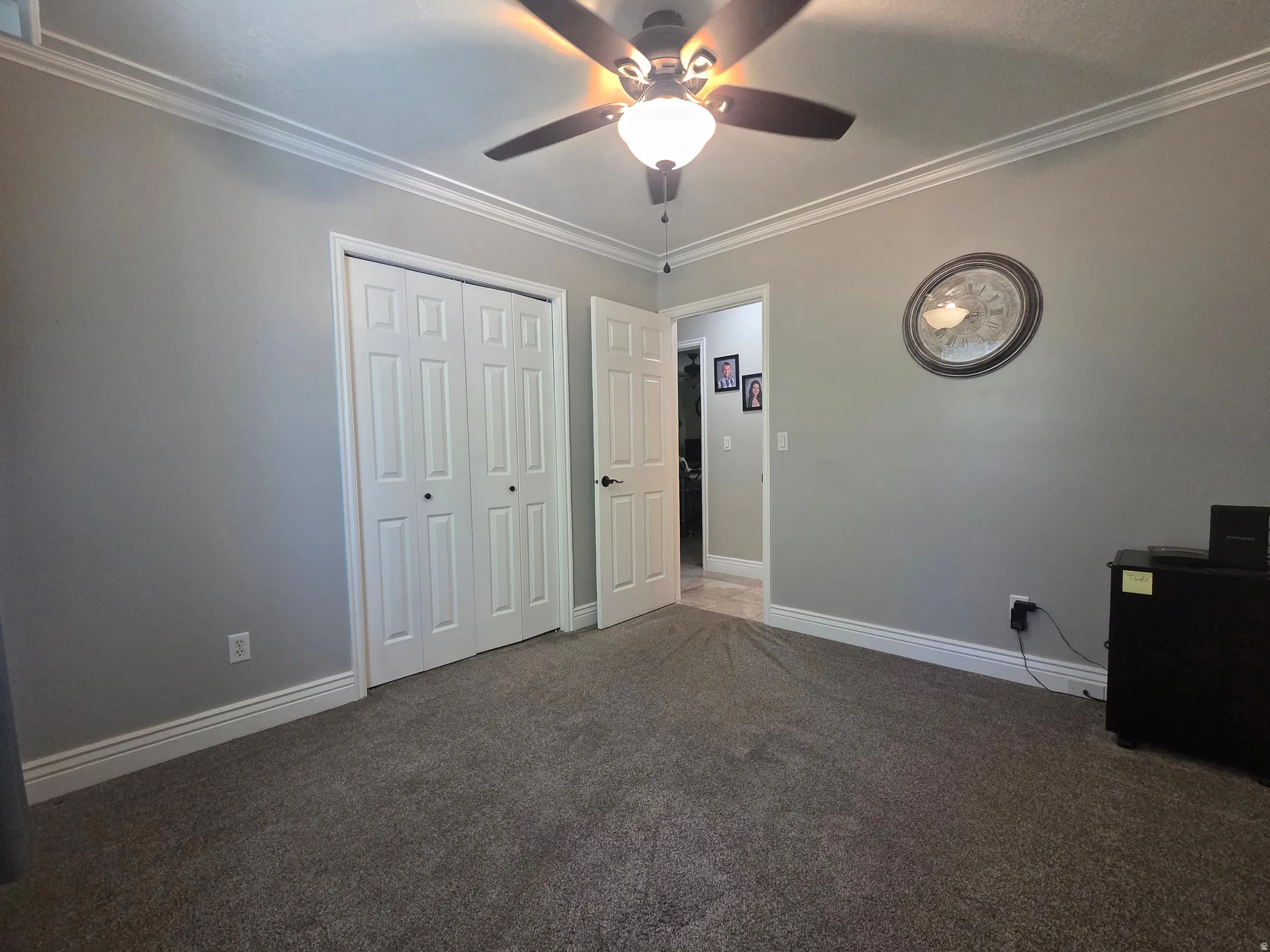 Carpeted room featuring crown molding, neutral wall paint, white baseboards, a ceiling fan with light fixture, and a built-in closet with bi-fold doors