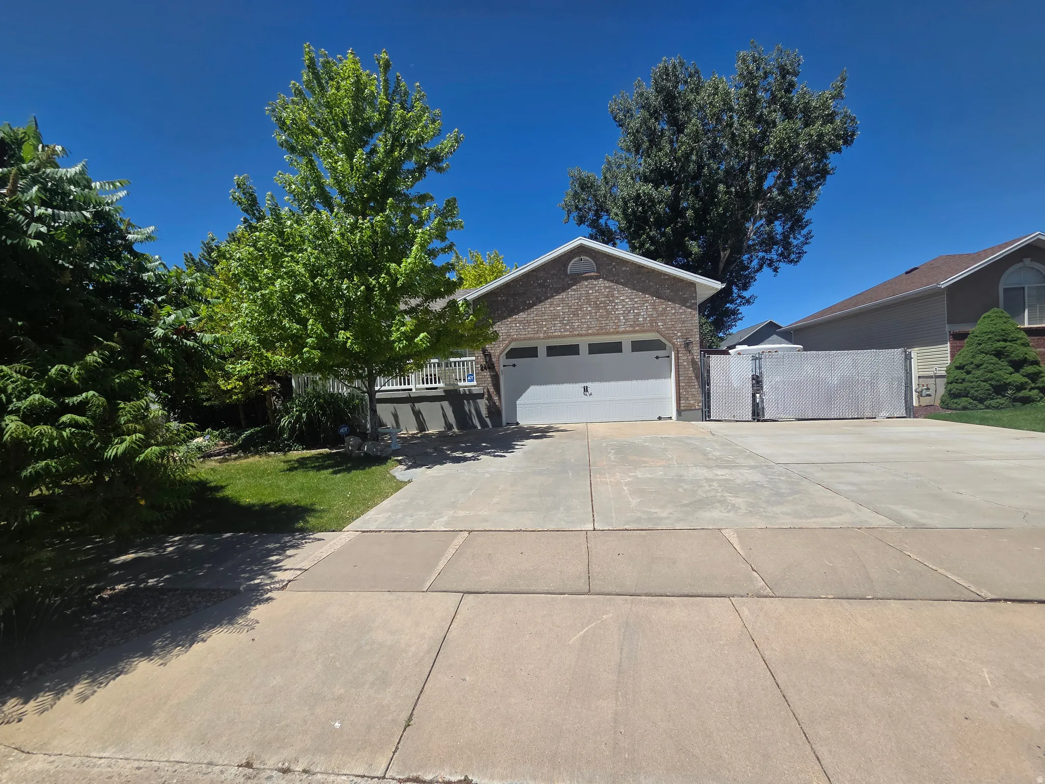 Brick-front residence featuring an attached two-car garage with a white door, a concrete driveway, and a white fence