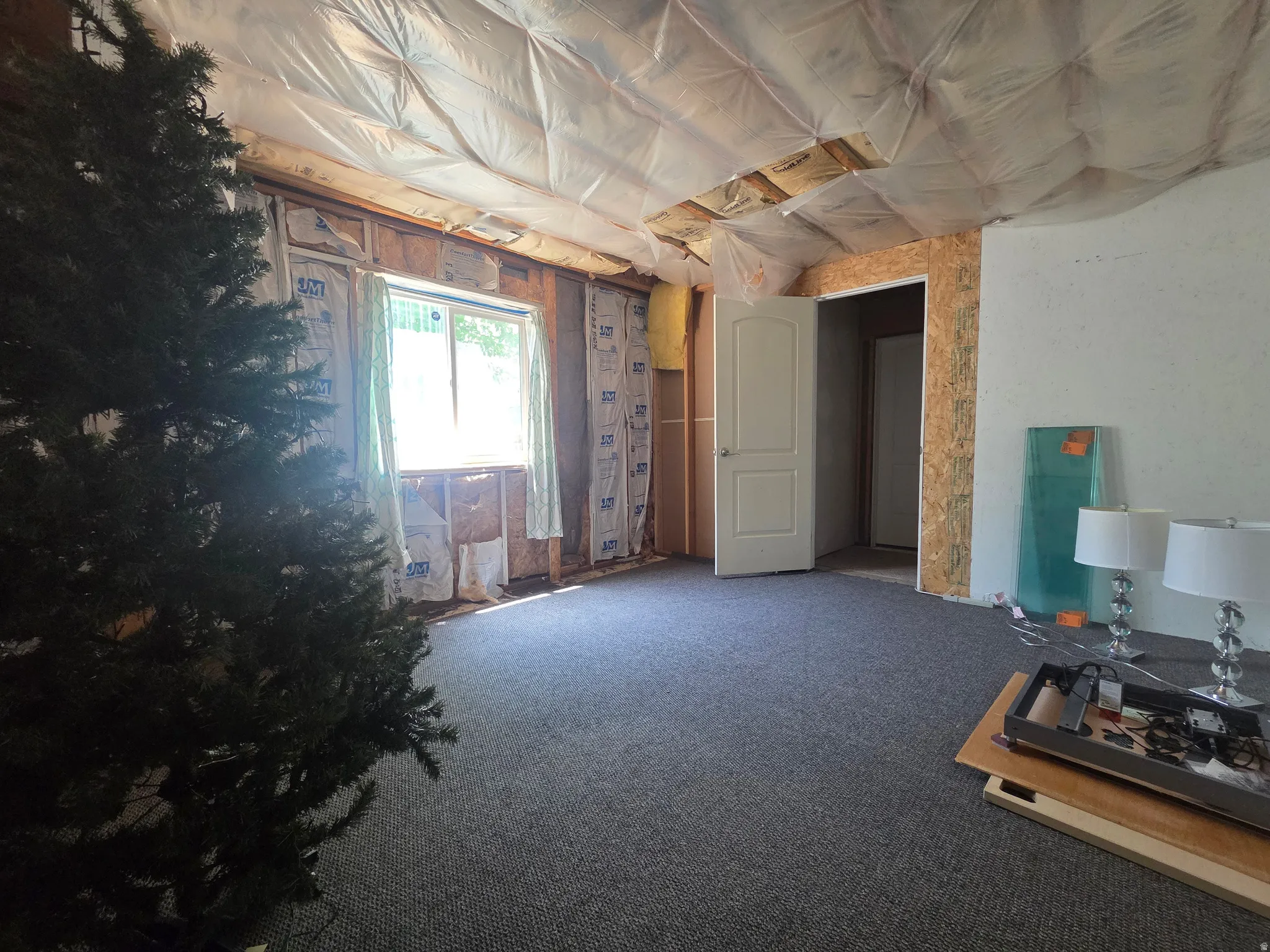 Room featuring exposed wall framing, a window with natural light, and a partially finished ceiling with insulation
