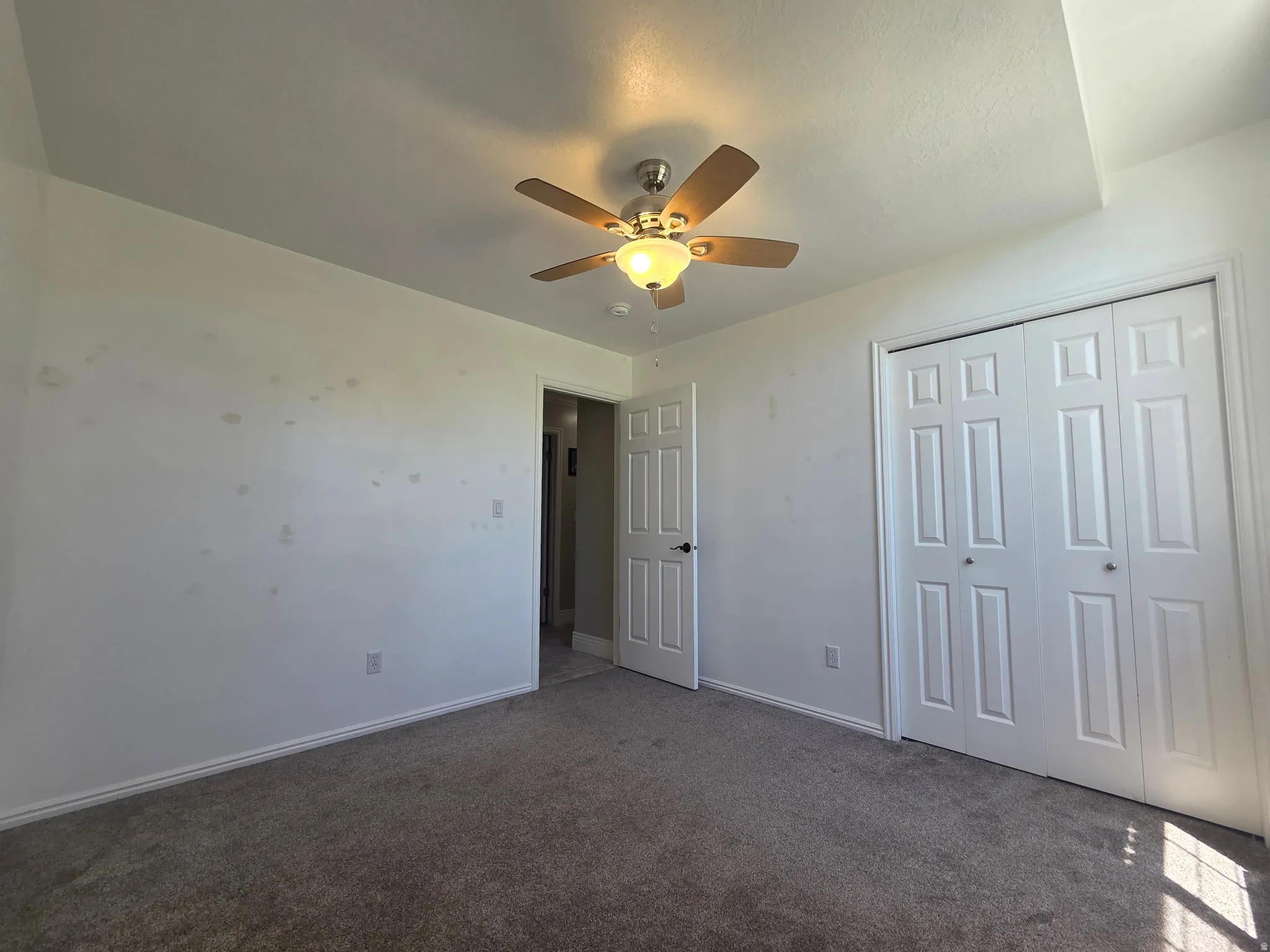 Carpeted interior space featuring a ceiling fan with integrated lighting, white painted walls, and a white two-panel bi-fold closet door
