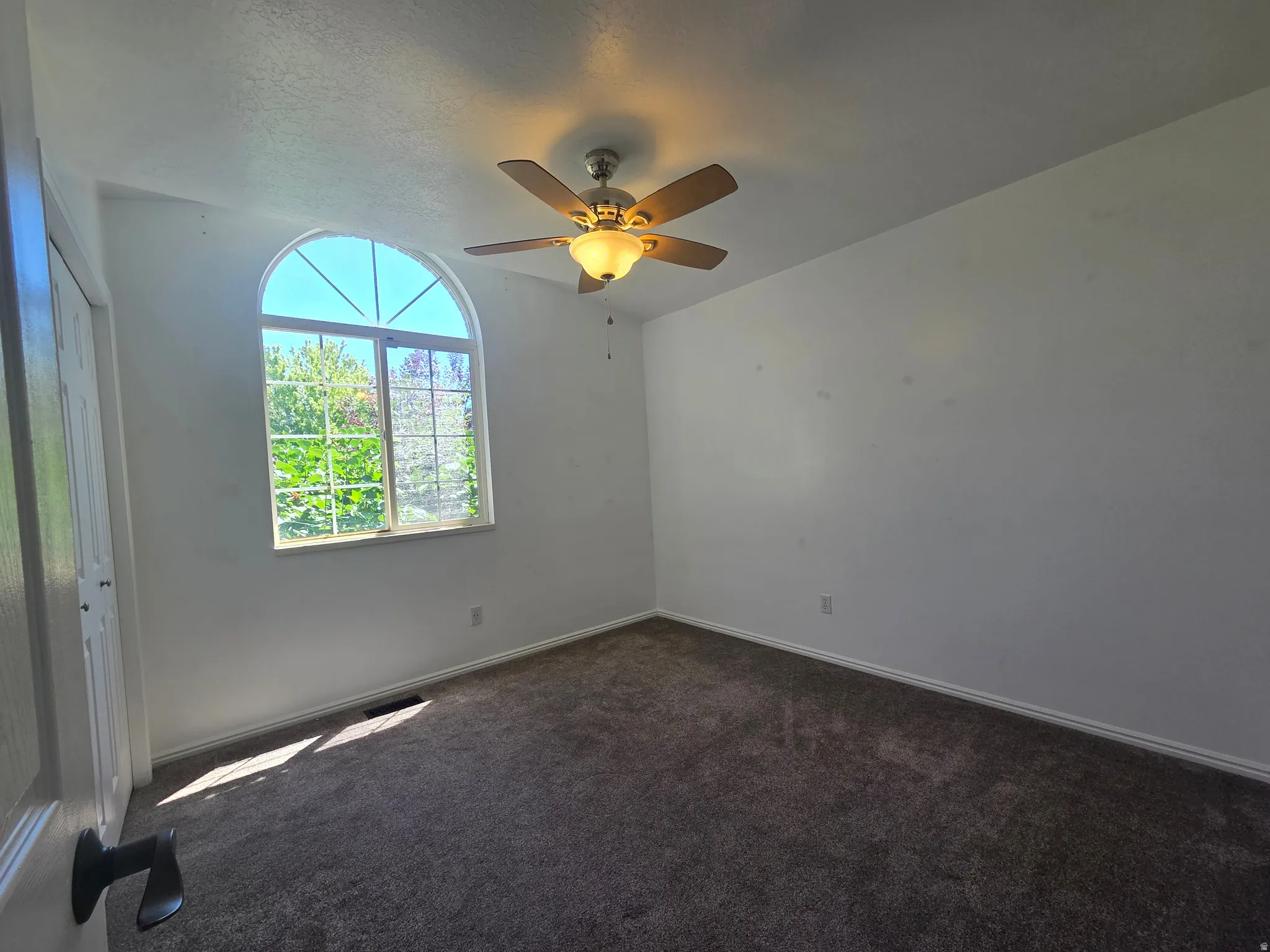 Room featuring a prominent arched window, dark gray carpet, a ceiling fan with light fixture, white walls, and white trim