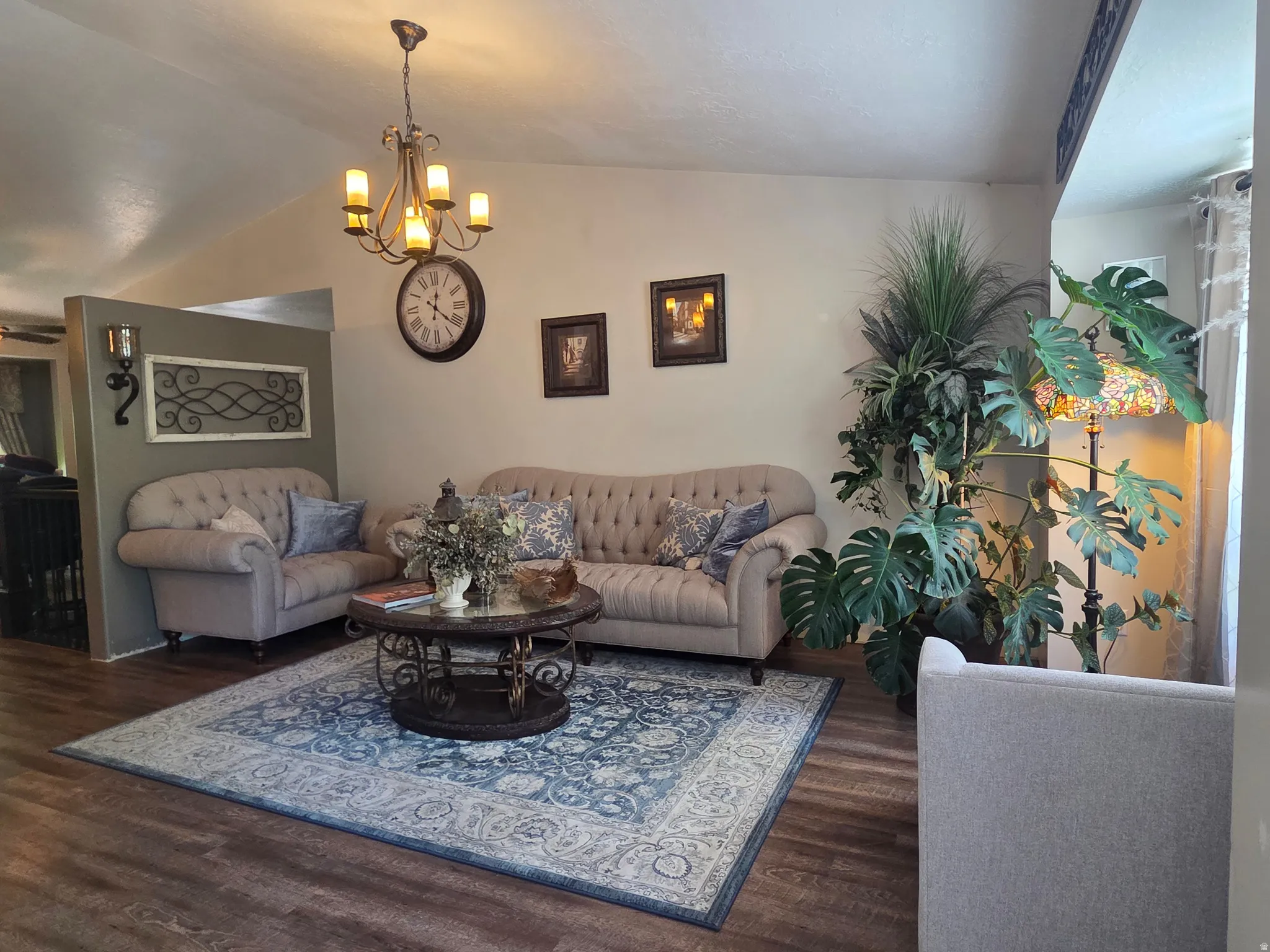 Living area featuring vaulted ceilings, wood-finish flooring, a decorative chandelier, and a partial wall with sconce lighting