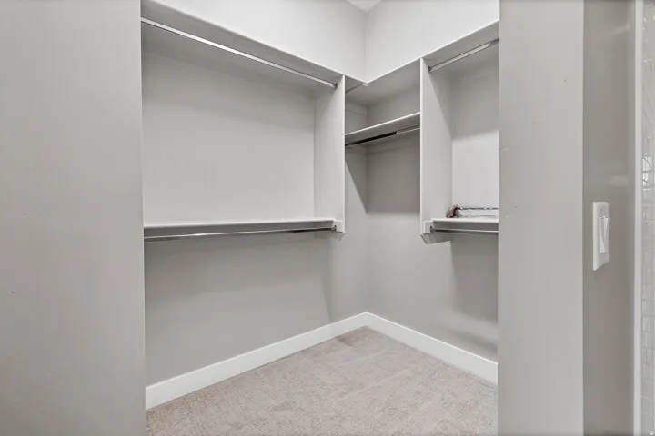 Walk-in closet featuring built-in shelving, chrome hanging rods, light gray walls, white baseboards, and light gray carpet