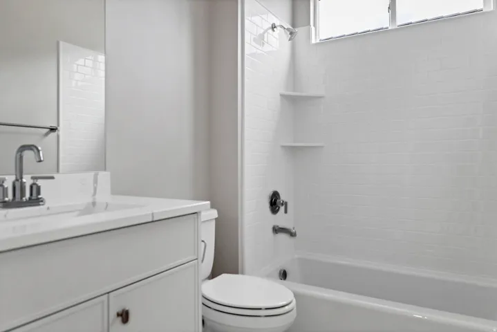 Bathroom featuring a white subway tile shower surround with integrated shelving and a white vanity with an integrated sink and chrome fixtures