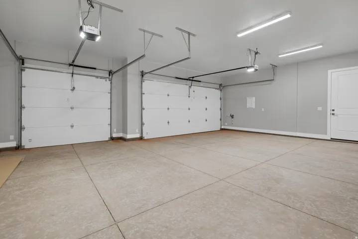 Two-car garage featuring a concrete floor, two white garage doors with automatic openers, overhead strip lighting, and a white interior access door