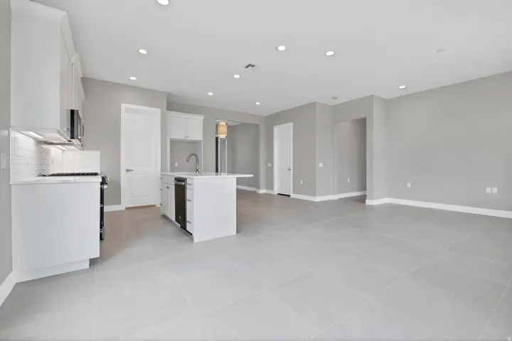 Open-concept living area featuring a kitchen with white cabinetry, a center island with sink, stainless steel appliances, and a subway tile backsplash