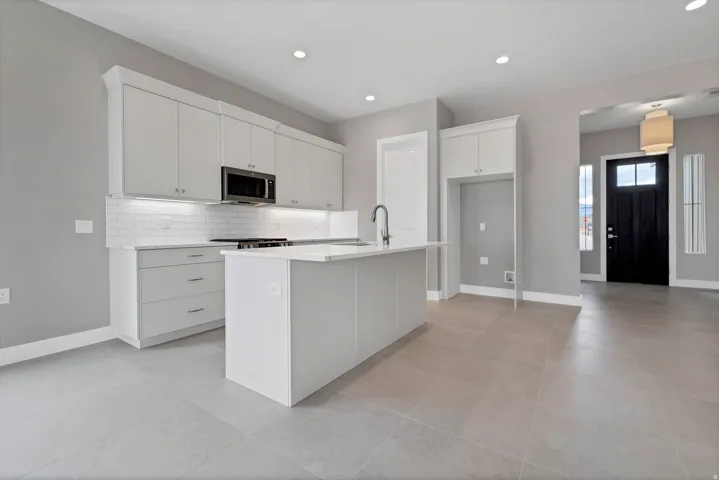 Modern kitchen featuring light gray cabinetry with sleek hardware, a central island with an undermount sink, and a white subway tile backsplash