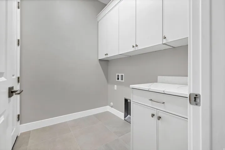 Utility room featuring extensive white cabinetry, a quartz countertop, and large format tile flooring