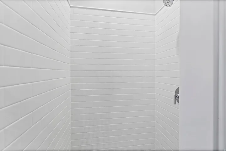 Shower enclosure featuring white subway tile walls, a rain showerhead, and a chrome single-handle control valve