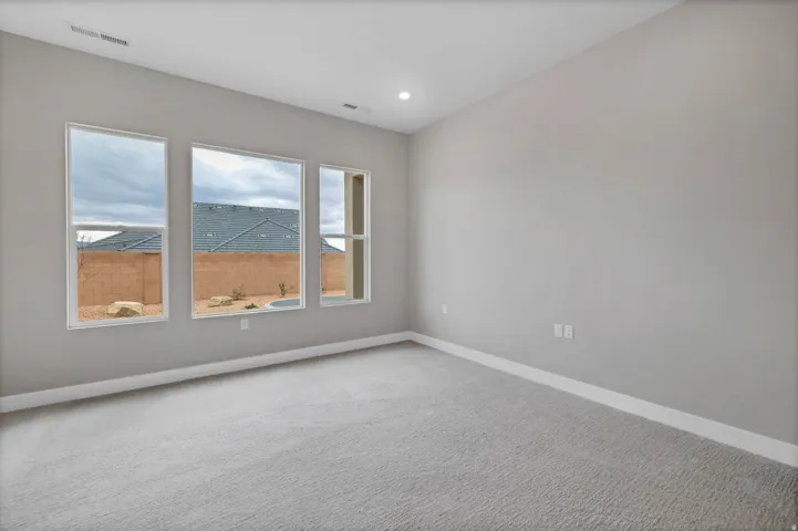 Spacious room featuring light gray walls, plush gray carpeting, white baseboards, and three vertical windows