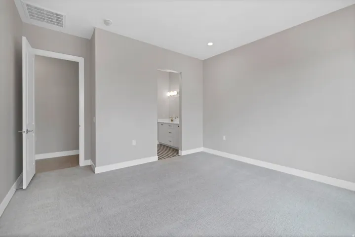 Spacious room featuring light gray walls, gray carpeting, and white baseboards, with an ensuite bathroom entrance