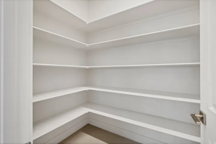 Spacious pantry featuring multiple tiers of white shelving, L-shaped lower shelving, and light-toned flooring