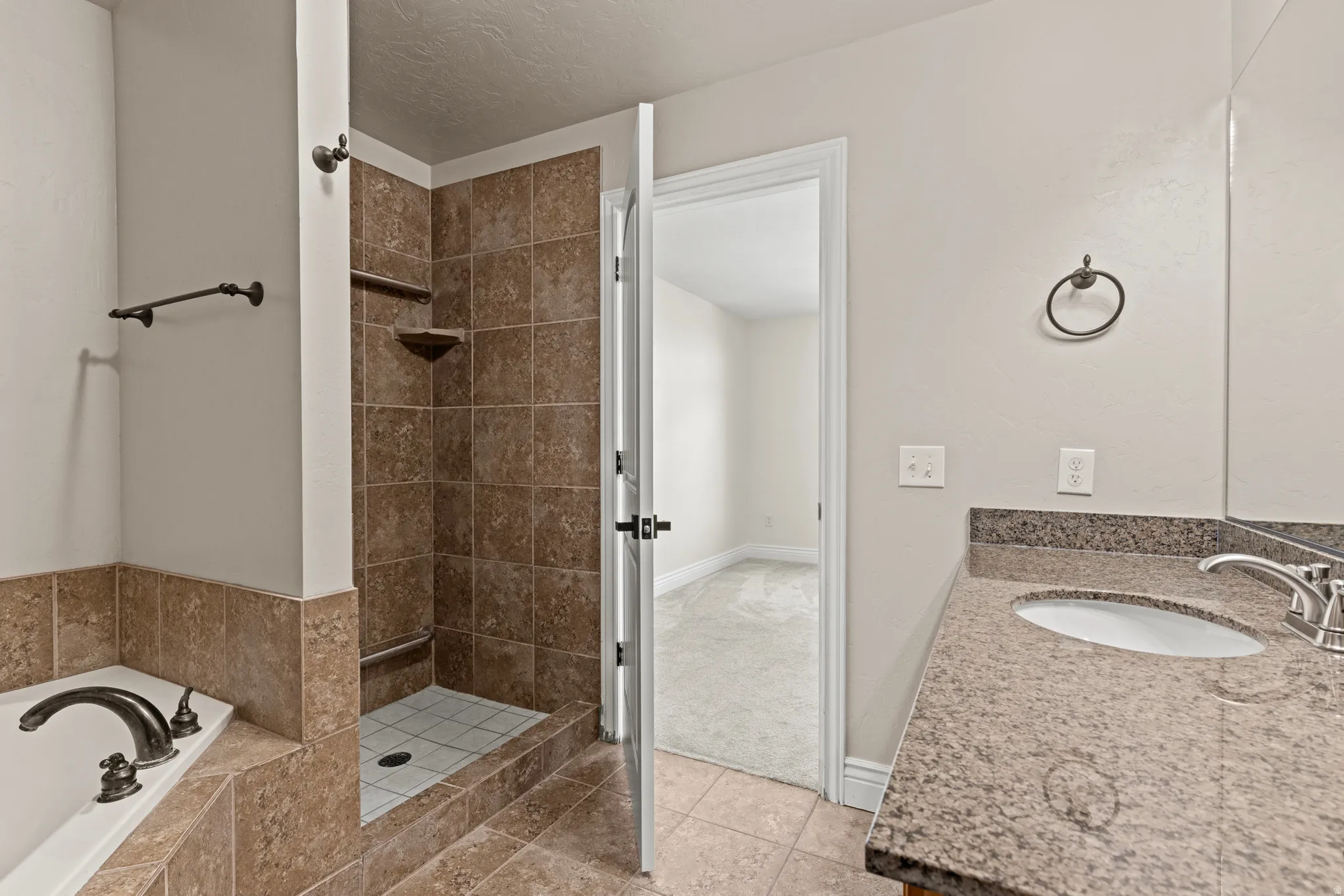Bathroom featuring a separate shower with brown tile surround and built-in shelving, a white soaking tub with dark bronze fixtures, and a vanity with a granite-style countertop and undermount sink