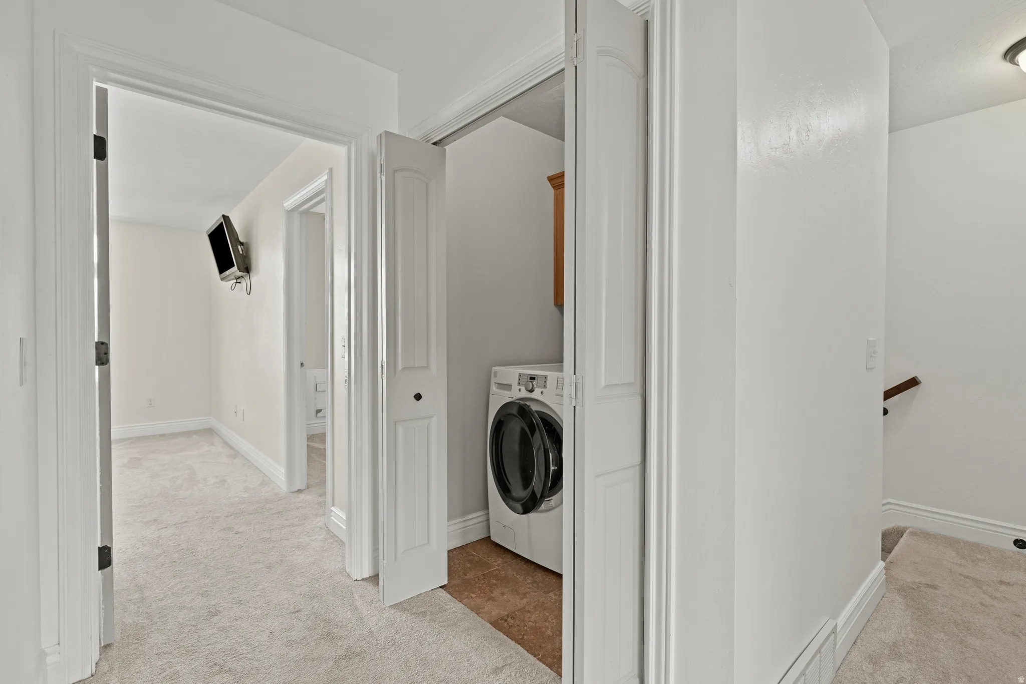 Hallway laundry closet with bi-fold doors, wood-finish flooring, and a built-in wood-tone cabinet