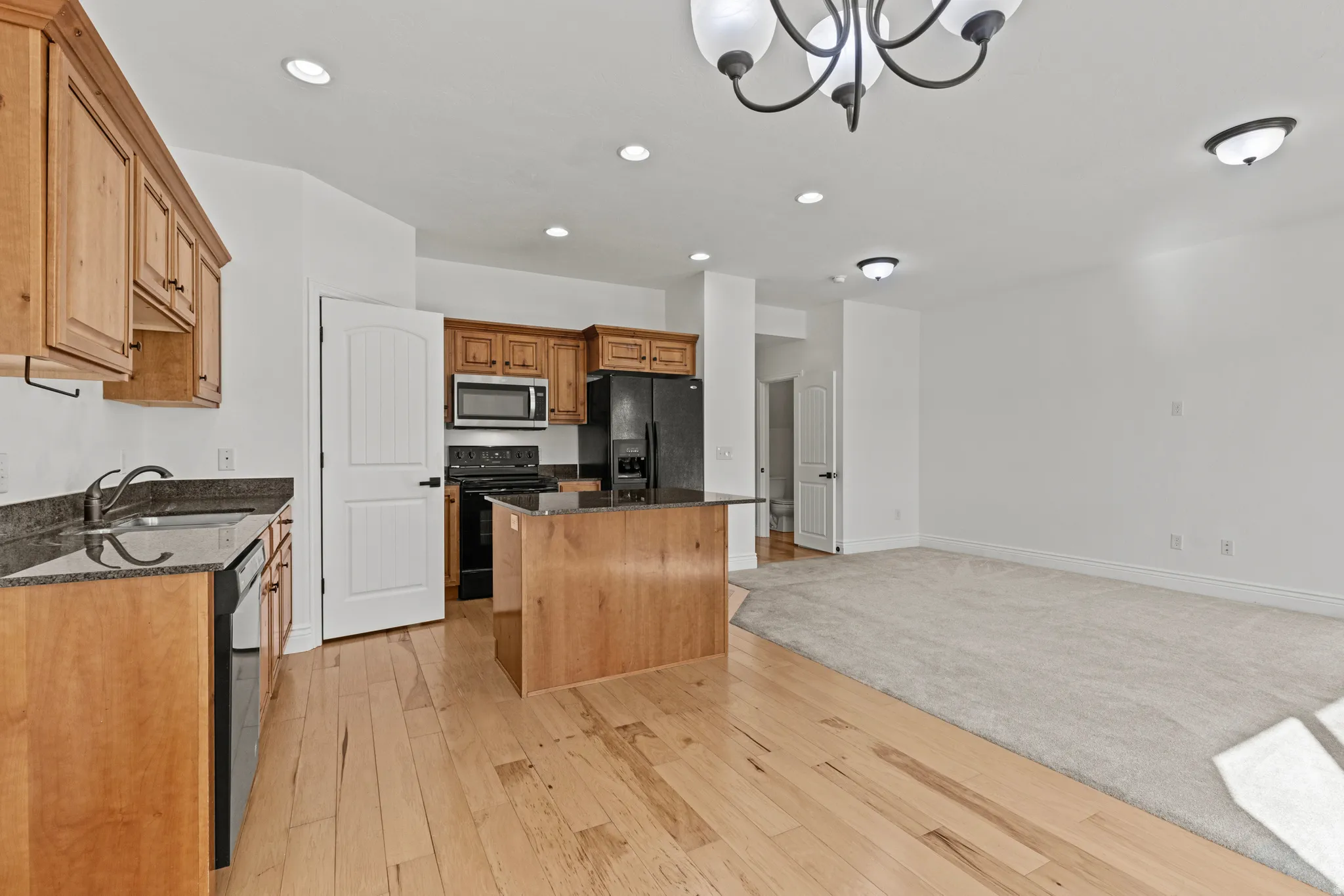 Open-concept living space featuring a kitchen with wood cabinetry, black appliances, dark countertops, and a central island